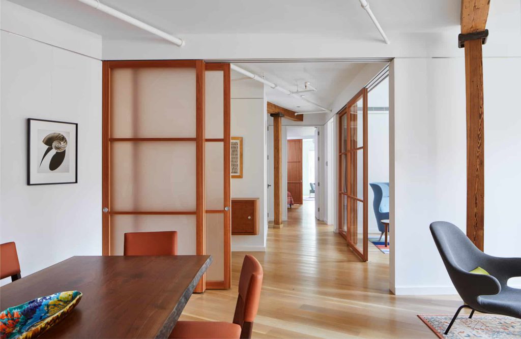 An open-concept interior featuring Raydoor sliding panels with wood frames and translucent inserts, separating a dining area from adjoining spaces while maintaining an open and cohesive design.