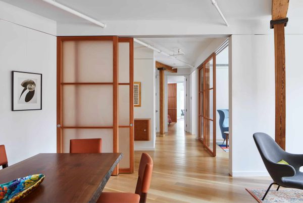 An open-concept interior featuring Raydoor sliding panels with wood frames and translucent inserts, separating a dining area from adjoining spaces while maintaining an open and cohesive design.