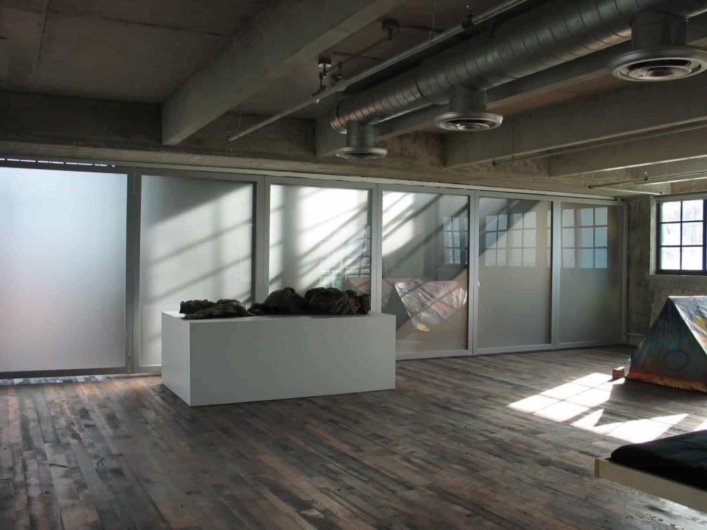 A stunning room dividing wall system divides an art gallery space while allowing ample natural light to filter through the frosted paneling.